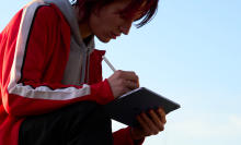a woman in a red jacket writing on an ipad air using an apple pencil