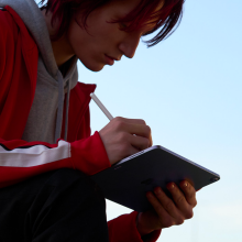 a woman in a red jacket writing on an ipad air using an apple pencil